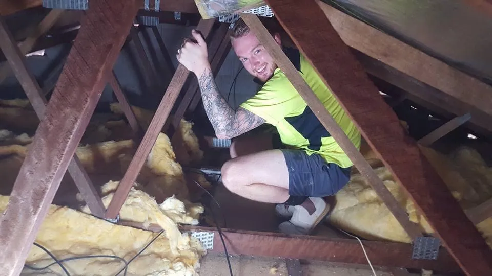 Ben photo from the roof space at Club Crocodile Airlie Beach. Working with a torch among timber rafters and fibreglass insulation. Grinning and loving the work.