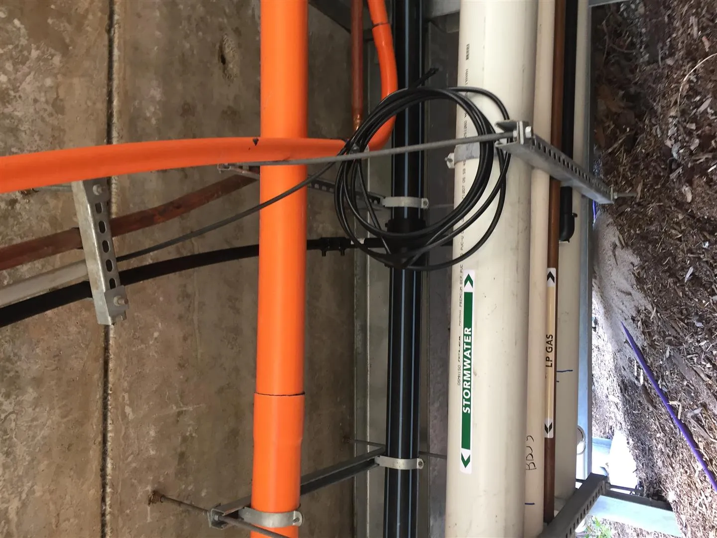 Comms hitching a ride on the suspended services run. With no easements and no underground option available, the telecommunications conduit was bracketed onto the same overhead services pathway carrying stormwater and LP gas across the precinct.